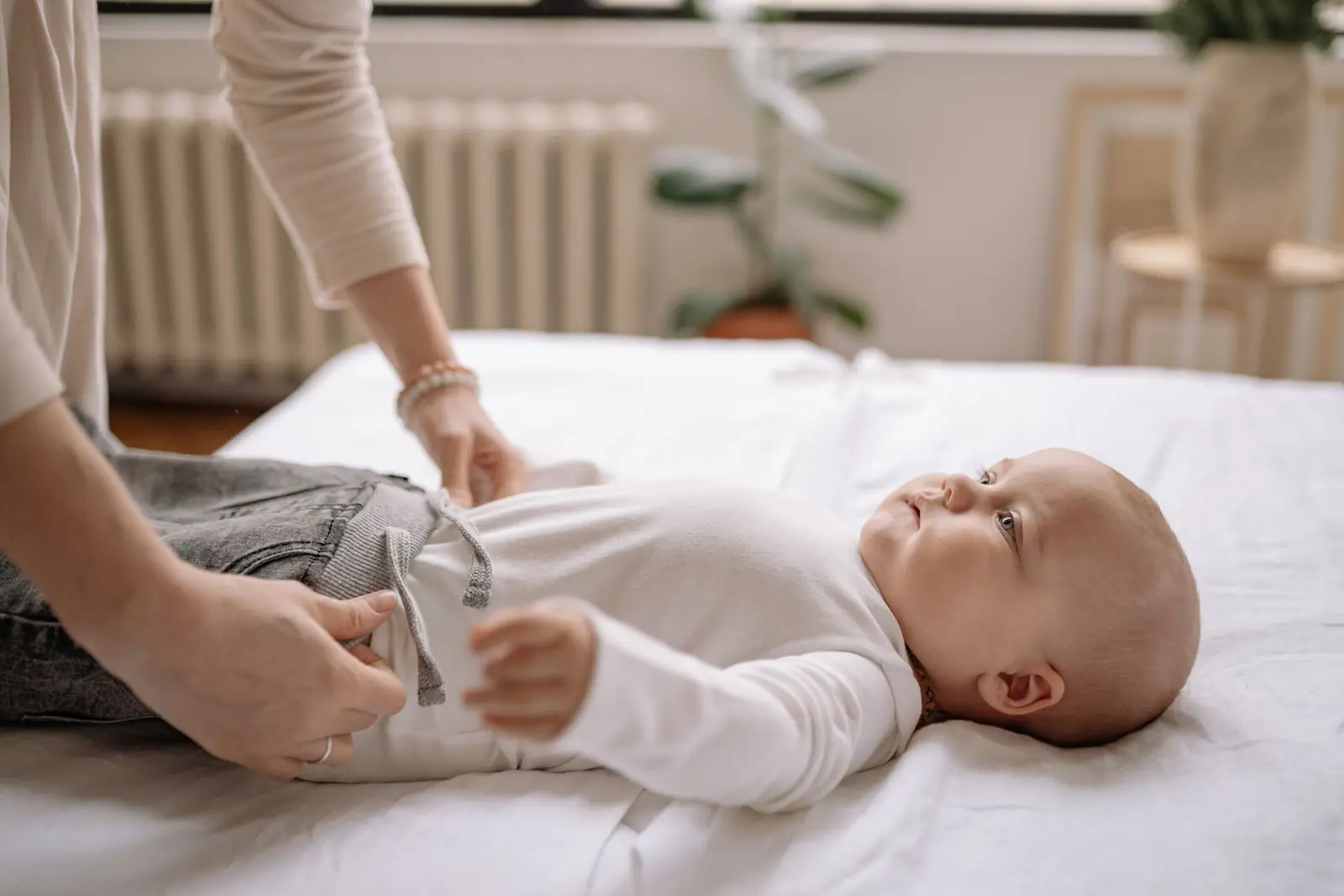 An adult fastening a garment on a baby lying on a padded changing surface