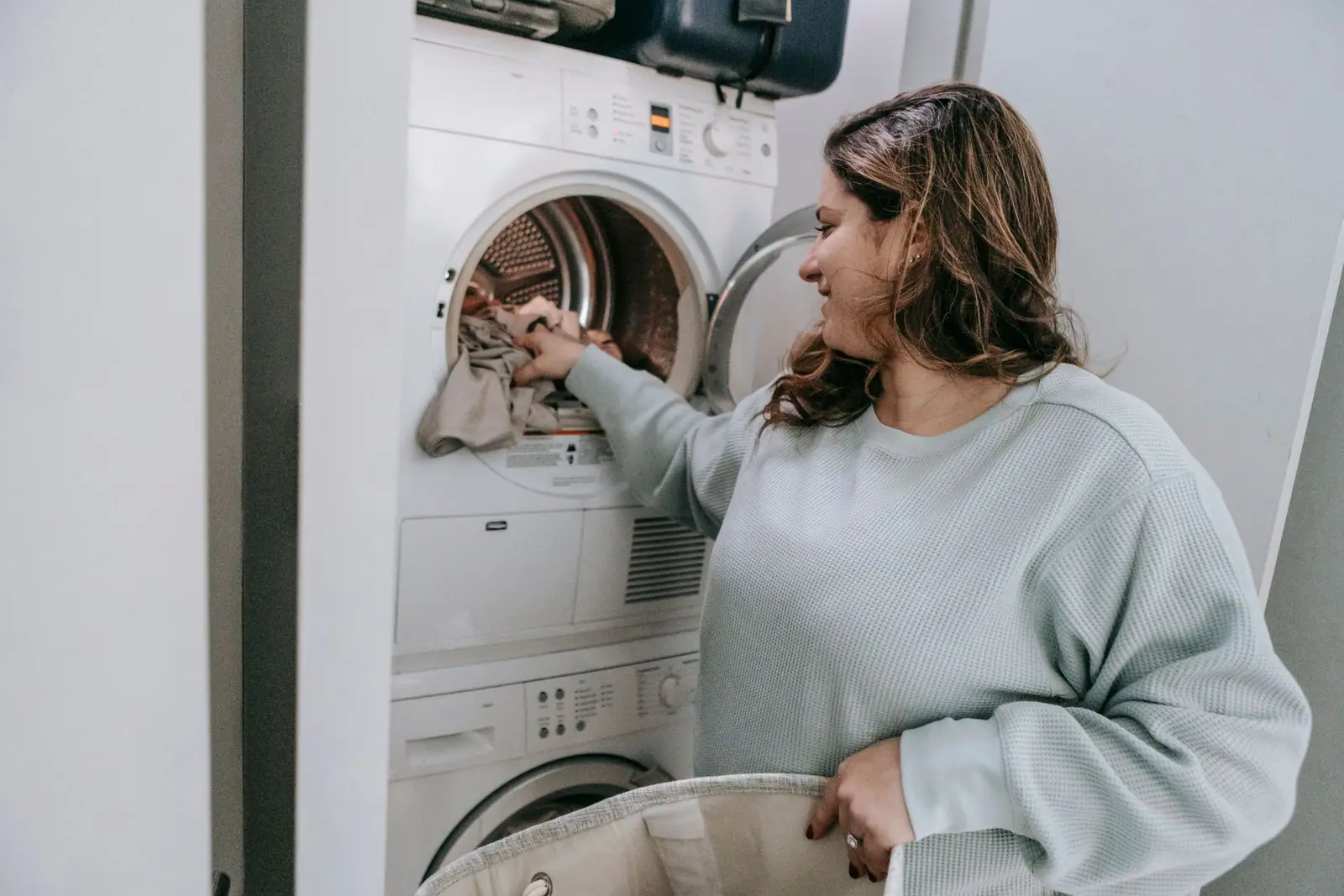 A woman beside a front-loading washing machine with its door open, holding folded laundry