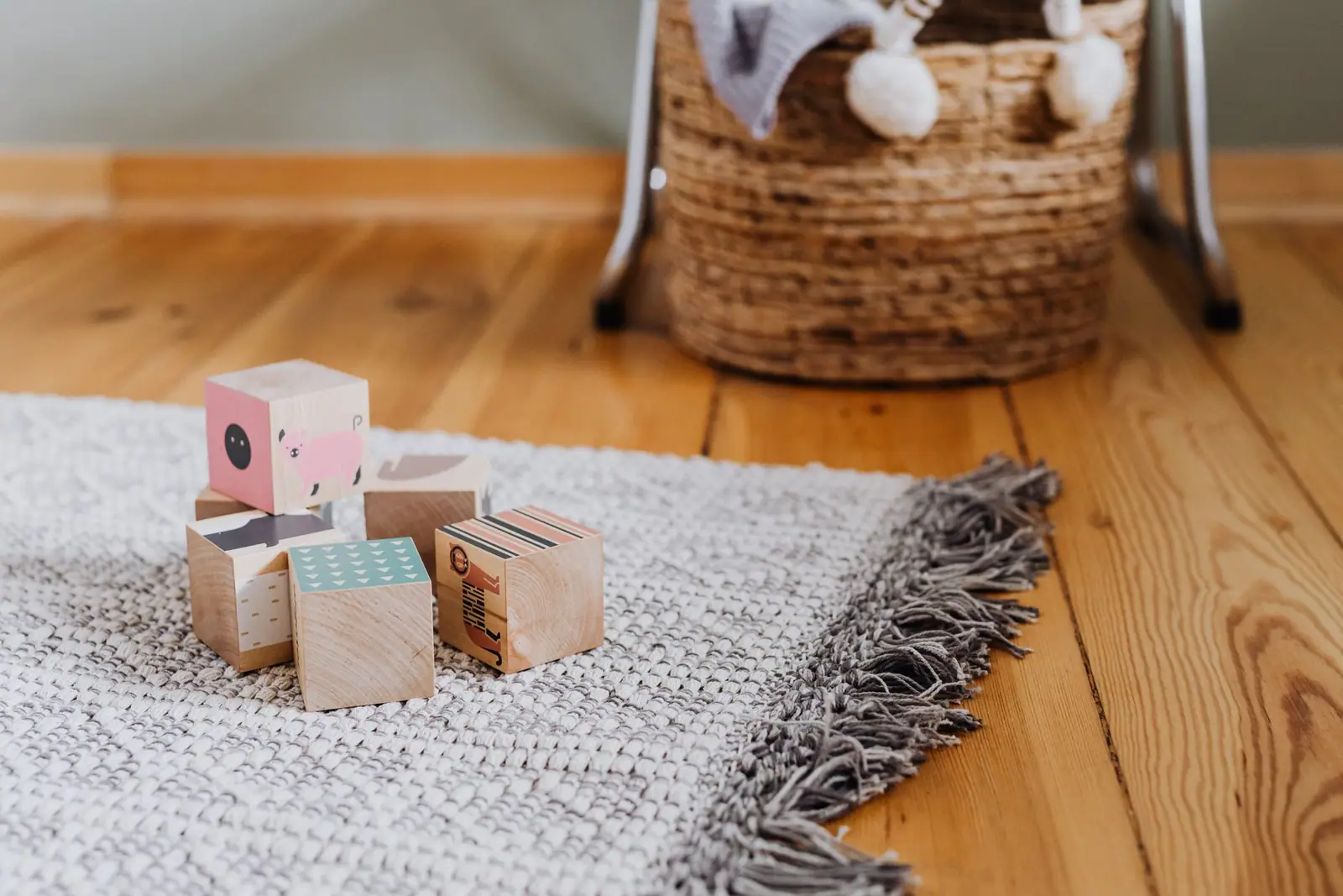 Three small wooden toy blocks on a rug beside a basket of toys