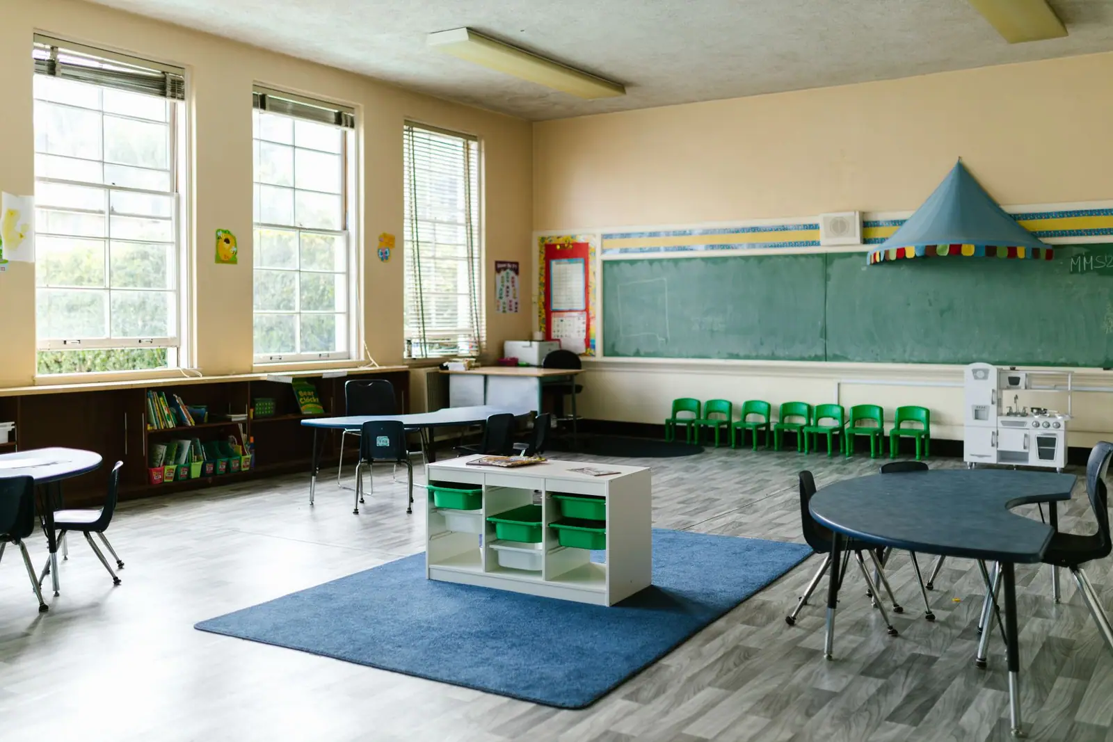 An empty childcare room with small tables, chairs and toy storage