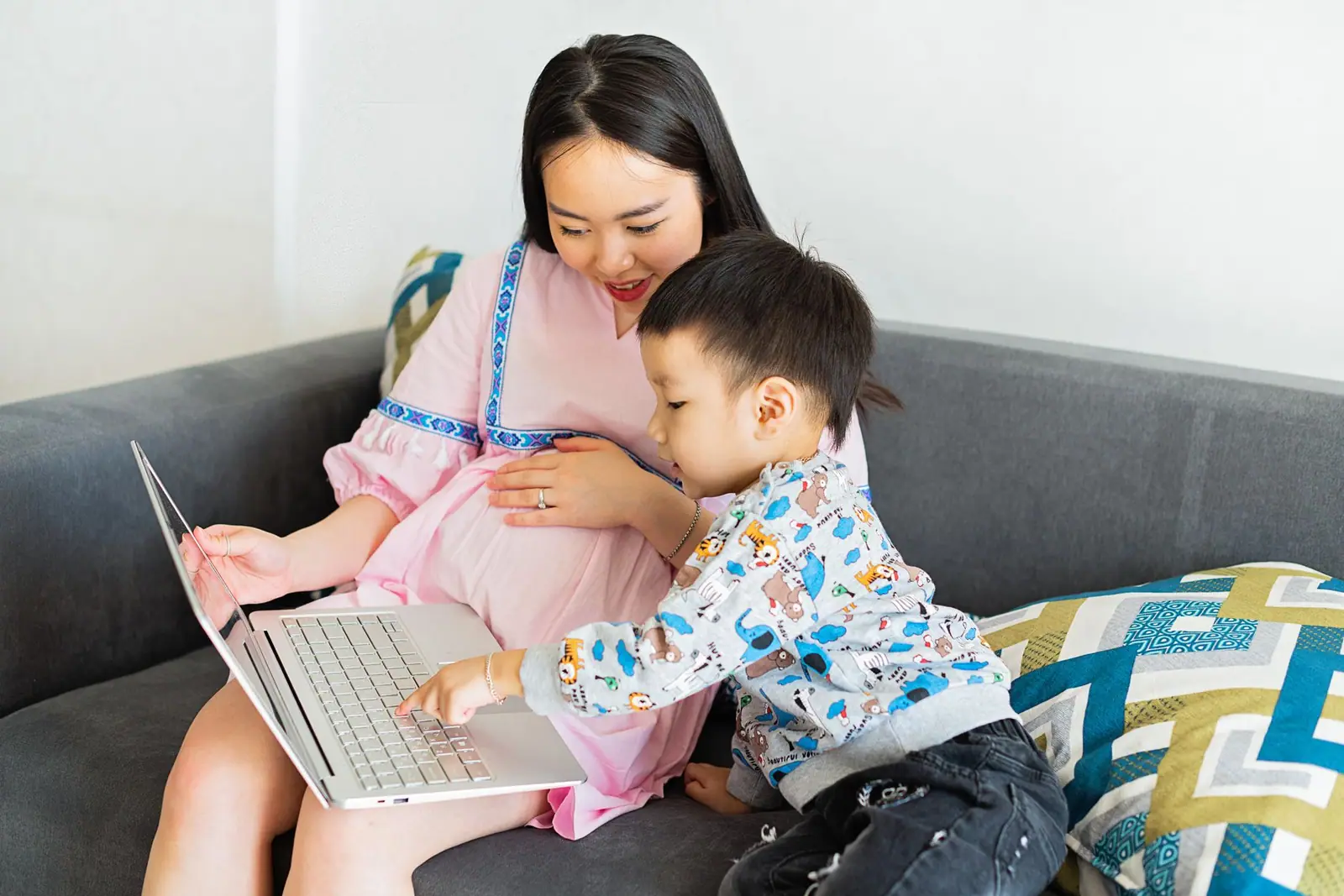 An adult and a young child looking at a laptop together on a sofa