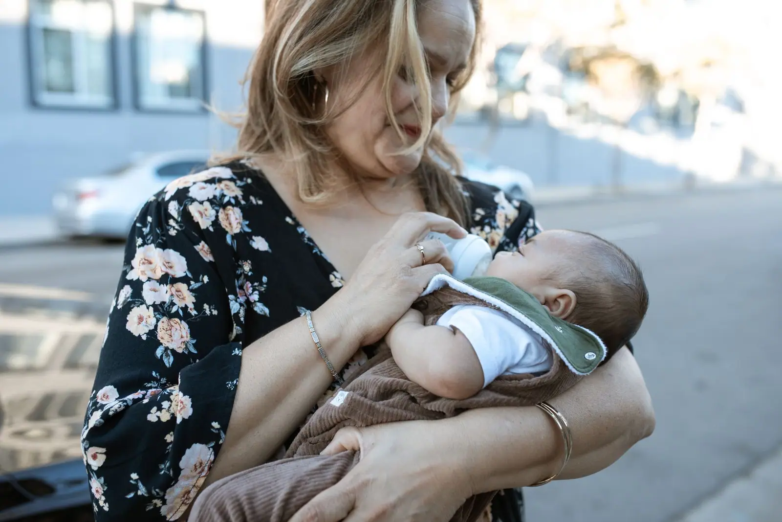 A seated adult bottle-feeding a baby outdoors