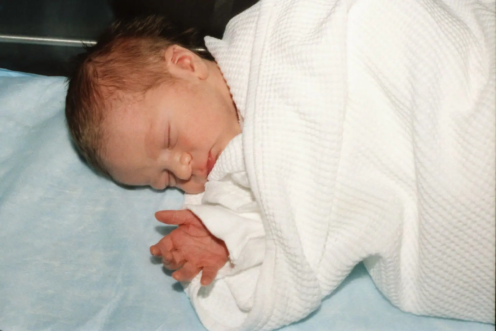 A newborn sleeping under a soft white blanket