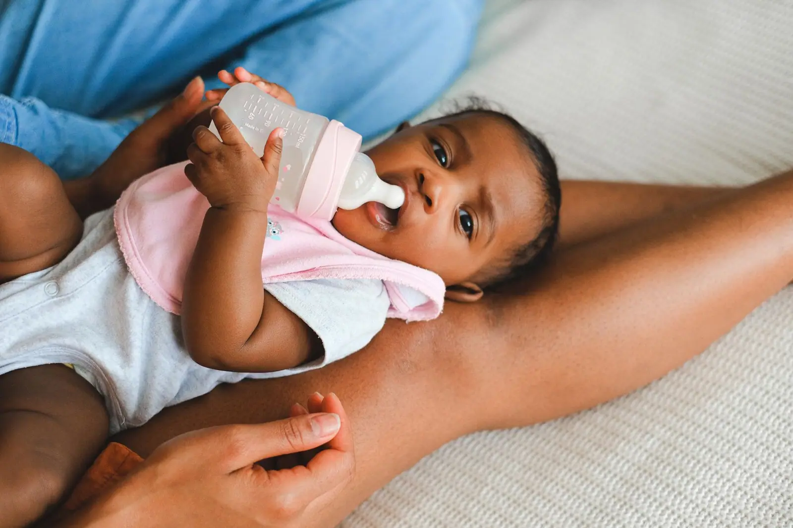 A baby held in an adult's arms while drinking from a feeding bottle